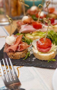 Parti farklı türde ekmek, sebze, peynir ve eti siyah taş tabakta yer..