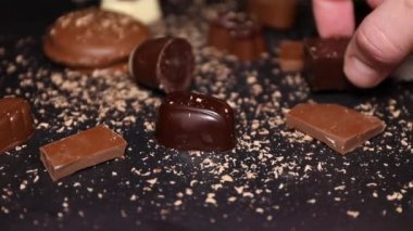 Çikolatalar, siyah bir tabakta sütlü çikolata parçaları ve çikolata şekeri alan bir el..