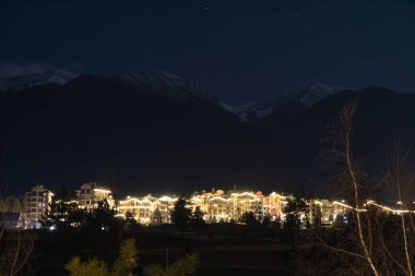 Razlog, Bulgaristan, 17 Şubat 2024. Pirin Golf 'ün otel kısmı ve geceleri ışıkları. Pirin Dağı 'nın zirveleri ve arka planda açık gökyüzü. Uzun pozlama.