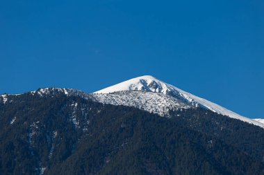 Arkasında karlı tepeler ve mavi gökyüzü olan dağ manzarasının yatay görüntüsü.