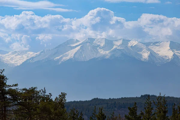 Arkasında karlı tepeler ve bulutlu gökyüzü olan dağ manzarasının yatay görüntüsü.