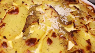 Sıcak patates tabağının üzerine rendelenmiş peynir. Peynir ve sıcak graten. İnce dilimlenmiş patates ve soğan ile yapılmış gratin patatesleri. Yozlaşmış, zengin ve kremalı çedar peynirinde pişmiş.