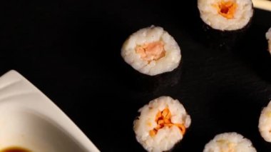 Dönen hosomaki suşi ruloları, soya sosu ve yemek çubukları.