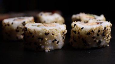 Suşi rulolarını siyah taş bir levha üzerinde somon salatası ve kızarmış siyah-beyaz susam tohumlarıyla kapatın.