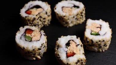 Yakın çekim, suşi rulolarının üst görüntüsü somon salatası ve kızarmış siyah-beyaz susam tohumları ile taş bir levha üzerinde, yavaş çekim