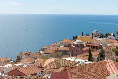 5 Nisan 2024. Kavala, Yunanistan. Eski kasabadaki evlerin üzerindeki çatılar ve güneşli bir günde güzel deniz..