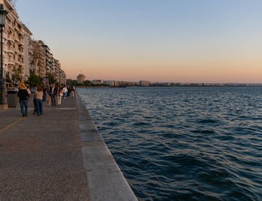 Selanik, Yunanistan, 23 Ekim 2024. Günbatımından sonra Selanik 'teki gezinti güvertesi, deniz ve tarihi kule.