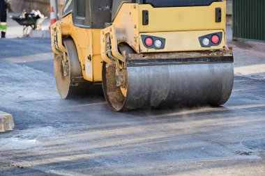 İnşaat alanında yol silindiri ve asfalt kaldırım makinesi, sıcak beton ve dumanla