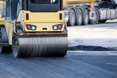 İnşaat alanında yol silindiri ve asfalt kaldırım makinesi, sıcak beton ve dumanla