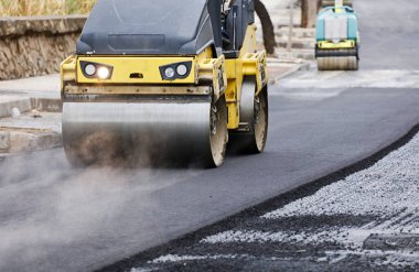 İnşaat alanında yol silindiri ve asfalt kaldırım makinesi, sıcak beton ve dumanla