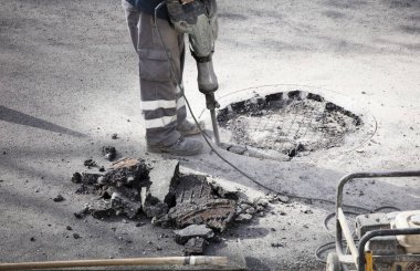 Asfalt işçisinin elindeki kaya matkabı yeraltında ve taşınabilir elektrik jeneratöründe çalışıyor.