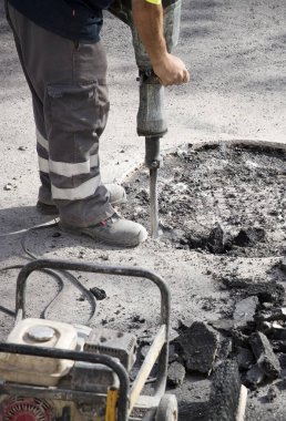Üniformalı bir operatörün elindeki hidrolik çekiç asfalt, hava kompresörü ve aletlerle çalışır.