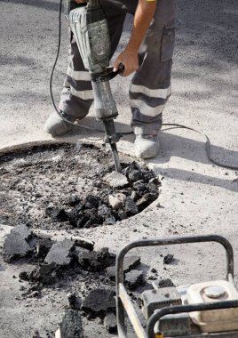 Üniformalı bir operatörün elindeki hidrolik çekiç asfalt, hava kompresörü ve aletlerle çalışır.