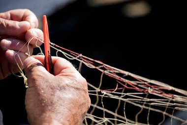 Balıkçıların elinde balıkçı ağı. Ağları iğne ve iplikle dikerek örüyor ve onarıyor.