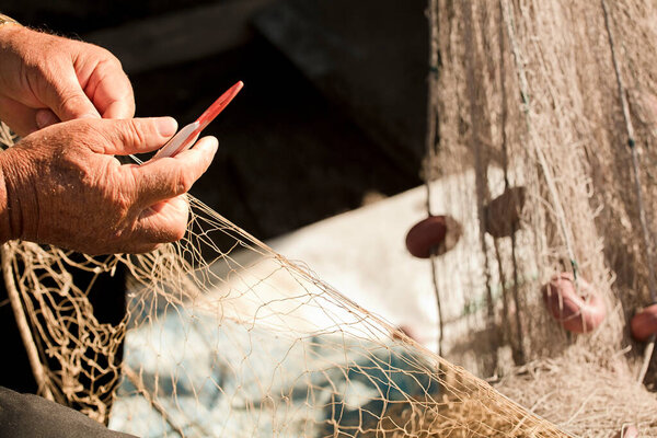 рыболовные сети в руках рыбака, он плетет и ремонтирует, шьет сети иголкой и ниткой