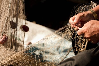 Balıkçıların elinde balık ağı, iğne ve iplikle, ayak parmaklarıyla ağı yakalıyor.