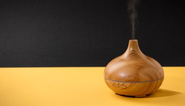 wooden air freshener with vapor of natural oil essences, yellow table with black background.