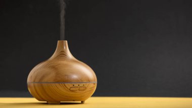 wooden air freshener with vapor of natural oil essences, yellow table with black background.