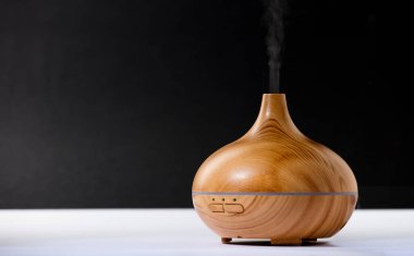 wooden air freshener with vapor of natural oil essences, white table black background.