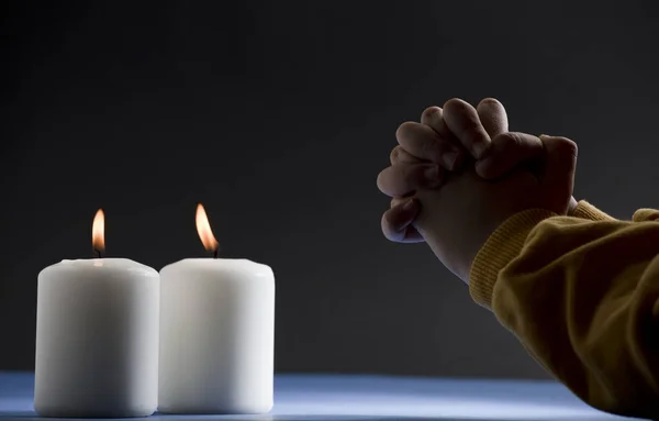 Мальчик Желтом Свитере Скрещенными Руками Молится Горящими Свечами Синий Стол — стоковое фото