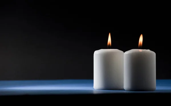 两只点燃着的蜡烛 都是一样的 放在蓝色的桌子上 背景是黑色的 — 图库照片