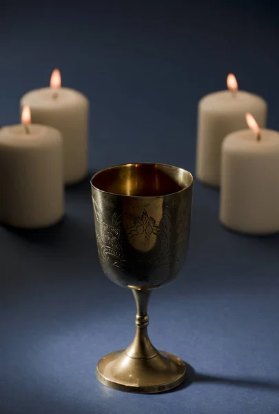 Golden chalice on altar with candles and flames, blue altar, dark brown background