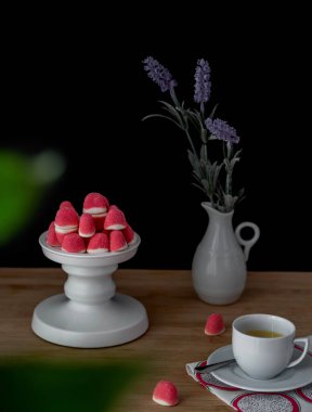 Beyaz kaidede pembe renkli marşmelov ve arka planda lavantalı vazo.