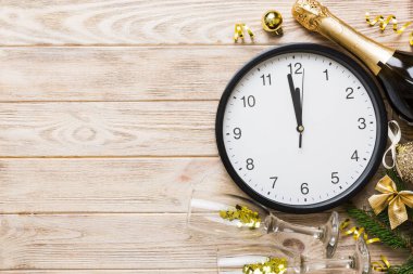 New year celebration concept with a bottle of champagne and two glasses toasting. Christmas gift box, alarm clock and fir tree branch on colored table. Top view Copy space.