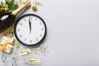 New year celebration concept with a bottle of champagne and two glasses toasting. Christmas gift box, alarm clock and fir tree branch on colored table. Top view Copy space.