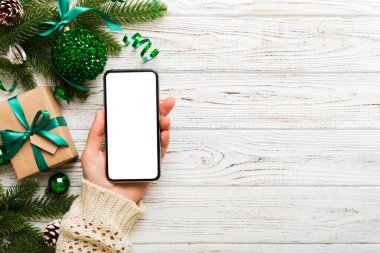 Mesaj atmak için yeri olan bir Noel modeli. Noel reklamı, uygulama şablonu. Masa arkasında boş ekran olan el ele tutuşan telefon. Mutlu yıllar ve Xmas Flat.