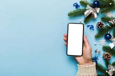 Mesaj atmak için yeri olan bir Noel modeli. Noel reklamı, uygulama şablonu. Masa arkasında boş ekran olan el ele tutuşan telefon. Mutlu yıllar ve Xmas Flat.