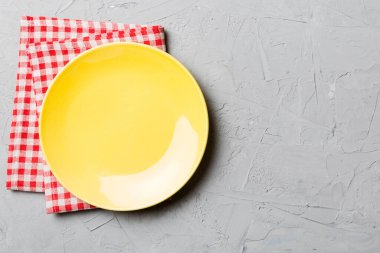 Renkli arka planda üst manzara. Yemek için masa örtüsü üzerinde boş yuvarlak sarı tabak. Tasarımınız için boşluk olan peçeteye boş tabak.