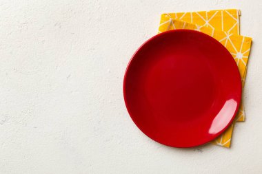 Renkli arka planda üst görünüm yiyecek için masa örtüsü üzerindeki boş yuvarlak kırmızı tabak. Tasarımınız için boşluk olan peçeteye boş tabak.