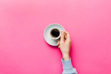 Renkli arka planda bir fincan kahve tutan minimalist stil bir kadın. Düz yerde, kapuçino bardağının üstünde. Metin için boş yer, kopyalama alanı. Kahve bağımlılığı. Üst manzara, düz uzanma.