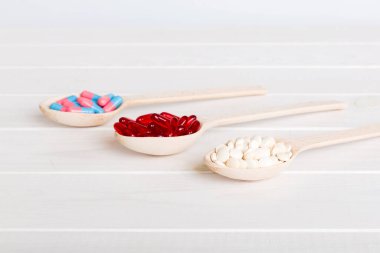 Renkli bir arka planda kaşıkta vitamin kapsülleri. Haplar sağlıklı bir yemek olarak sunuldu. Kırmızı yumuşak jel vitamin takviye kapsülleri kaşık üzerinde.