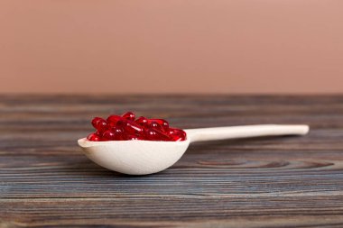 Vitamin capsules in a spoon on a colored background. Pills served as a healthy meal. Red soft gel vitamin supplement capsules on spoon.