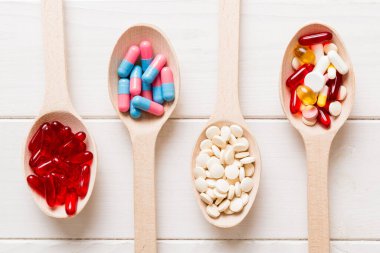Vitamin capsules in a spoon on a colored background. Pills served as a healthy meal. Red soft gel vitamin supplement capsules on spoon.