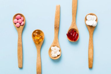 Renkli bir arka planda kaşıkta vitamin kapsülleri. Haplar sağlıklı bir yemek olarak sunuldu. Kırmızı yumuşak jel vitamin takviye kapsülleri kaşık üzerinde.