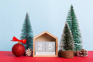 25 december. Christmas composition on colored background with a wooden calendar, with a gift box, toys, bauble copy space.