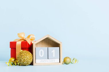 1 january. Christmas composition on colored background with a wooden calendar, with a gift box, toys, bauble copy space.