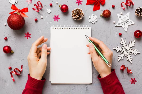 stock image Woman writing Christmas to do list on notebook on colored background with xmas decorations.