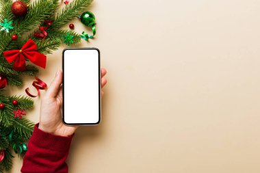 Mesaj atmak için yeri olan bir Noel modeli. Noel reklamı, uygulama şablonu. Masa arkasında boş ekran olan el ele tutuşan telefon. Mutlu yıllar ve Xmas Flat.