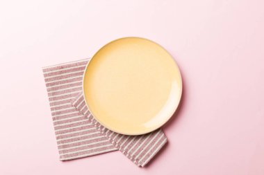 Renkli arka planda üst manzara. Yemek için masa örtüsü üzerinde boş yuvarlak sarı tabak. Tasarımınız için boşluk olan peçeteye boş tabak.