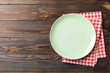 Renkli arka planda üst görünüm yiyecek için masa örtüsünün üzerinde boş yuvarlak yeşil tabak. Tasarımınız için boşluk olan peçeteye boş tabak.