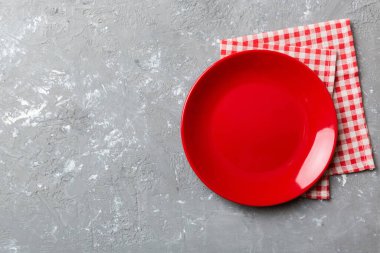 Renkli arka planda üst görünüm yiyecek için masa örtüsü üzerindeki boş yuvarlak kırmızı tabak. Tasarımınız için boşluk olan peçeteye boş tabak.