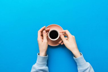 Renkli arka planda bir fincan kahve tutan minimalist stil bir kadın. Düz yerde, kapuçino bardağının üstünde. Metin için boş yer, kopyalama alanı. Kahve bağımlılığı. Üst manzara, düz uzanma.