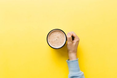 Renkli arka planda bir fincan kahve tutan minimalist stil bir kadın. Düz yerde, kapuçino bardağının üstünde. Metin için boş yer, kopyalama alanı. Kahve bağımlılığı. Üst manzara, düz uzanma.
