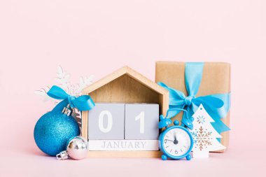 1 january. Christmas composition on colored background with a wooden calendar, with a gift box, toys, bauble copy space.