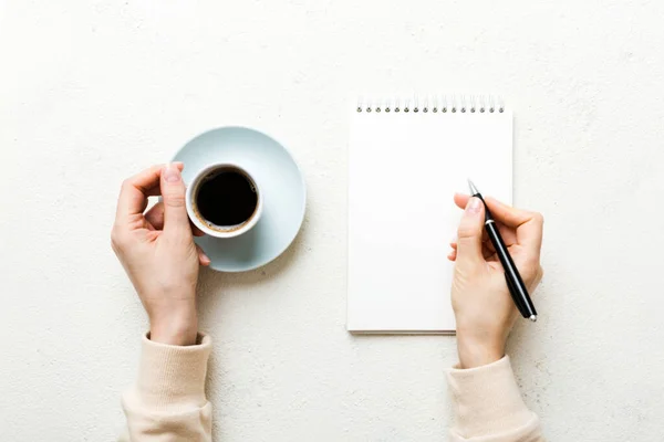 Woman hand with pencil writing on notebook and hold coffee cup. Woman working on office table with coffee.