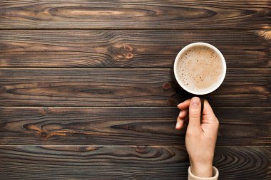 Renkli arka planda bir fincan kahve tutan minimalist stil bir kadın. Düz yerde, kapuçino bardağının üstünde. Metin için boş yer, kopyalama alanı. Kahve bağımlılığı. Üst manzara, düz uzanma.